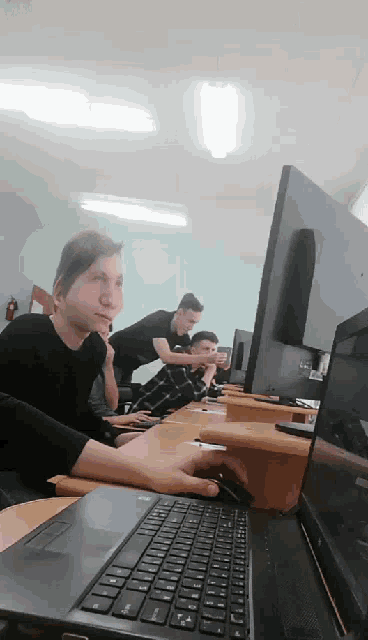 a group of people are sitting in front of computers and one of them is typing on a laptop