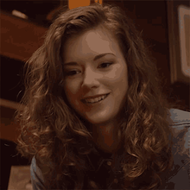 a woman with long curly hair is smiling and wearing a blue shirt