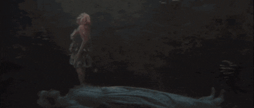 a woman in a dress is standing on a rock in the dark looking at fish .