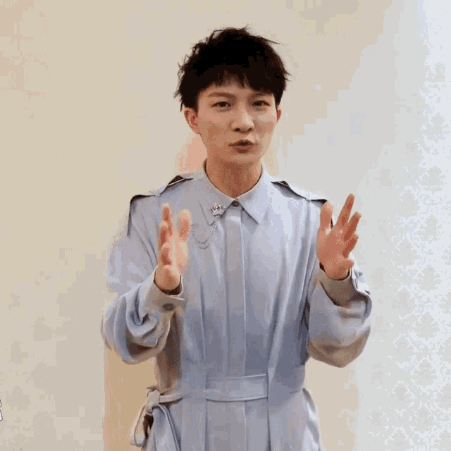a young man wearing a light blue shirt is making a peace sign with his hands