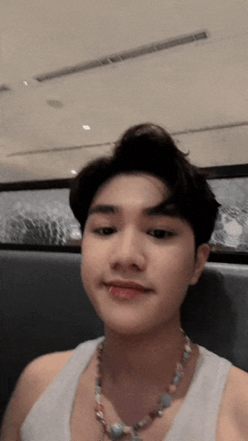 a young man wearing a white tank top and a necklace looks at the camera .