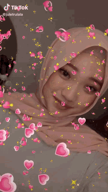 a woman wearing a hijab is surrounded by pink hearts and says tik tok