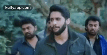 a man with a beard is walking with a group of men in a forest .