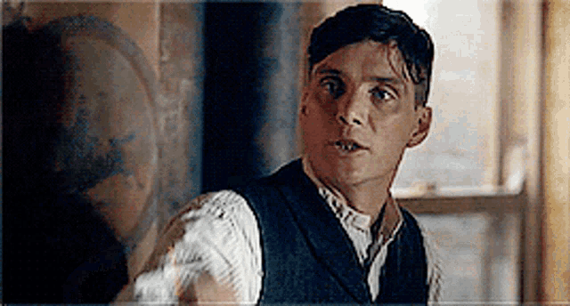 a man in a vest is standing in front of a window and looking at something .