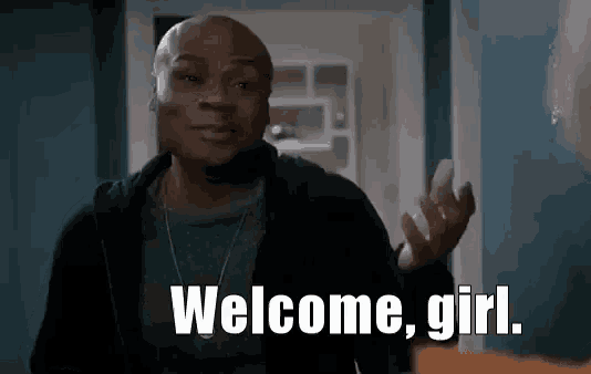 a man is standing in a hallway talking to a woman and says `` welcome , girl . ''