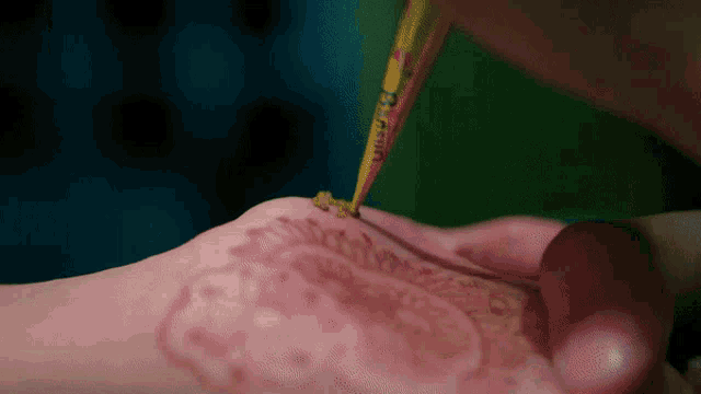 a person is applying henna to another person 's hand with a cone that says ' henna ' on it
