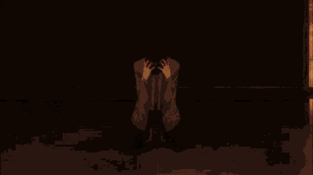 a man in a suit and tie is kneeling down with his hands on his head .