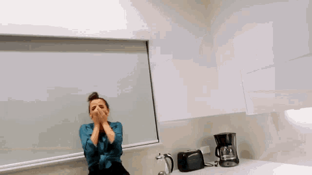 a woman covering her mouth while sitting on a counter in front of a window