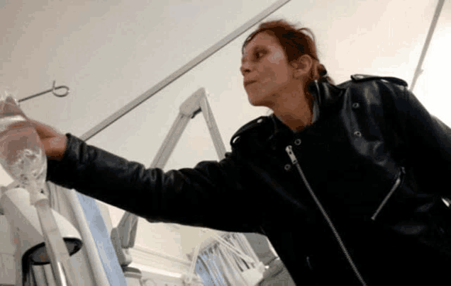 a woman in a black leather jacket is holding a bag of liquid in her hand .