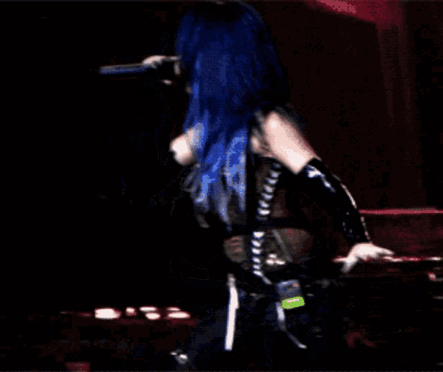 a woman with blue hair is singing into a microphone on a stage