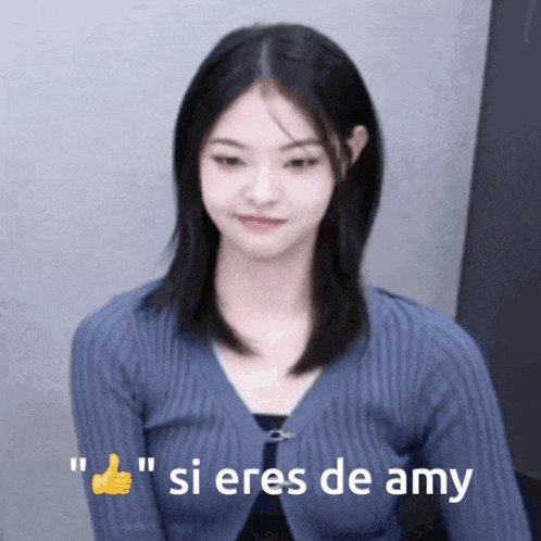 a girl in a blue sweater is giving a thumbs up