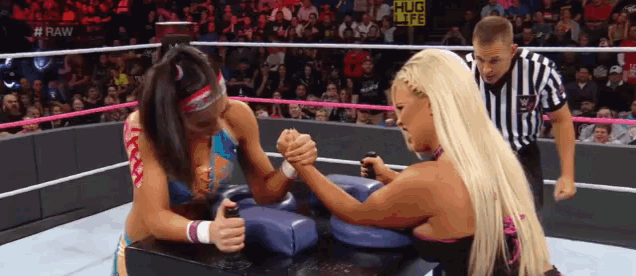 two women arm wrestling in a wrestling ring with a referee in the background