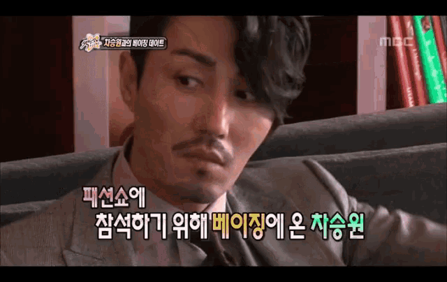 a man in a suit and tie is sitting on a couch with korean writing on the bottom of the screen