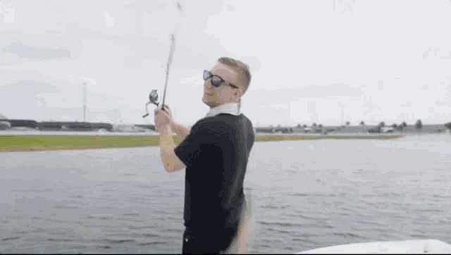 a man is fishing on a boat in the water while wearing sunglasses .