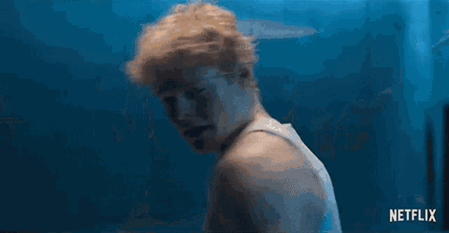 a man in a tank top is standing in a room with a blue wall .