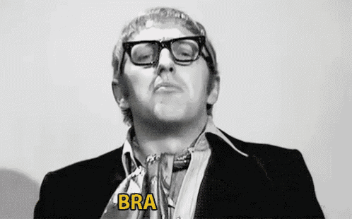 a man wearing glasses and a suit is making a funny face and saying bra vo .