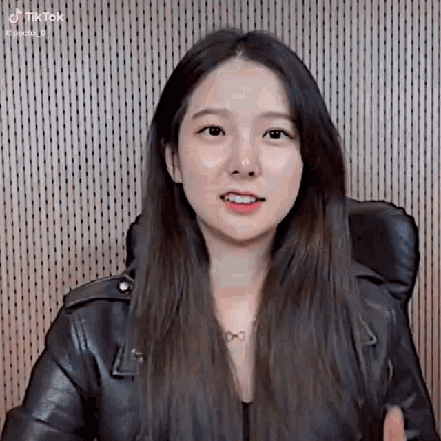 a woman in a leather jacket is sitting in a chair .