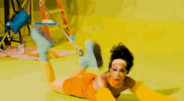 a woman is laying on her stomach on a yellow floor with a ladder in the background