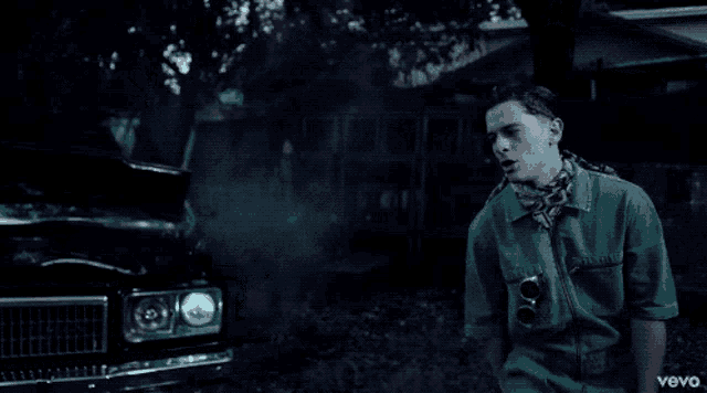 a man in a green shirt stands in front of a black car with the word vevo on the bottom