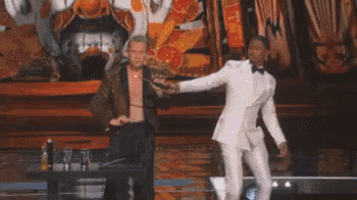 a man in a white suit is dancing in front of a fireball coming out of his mouth