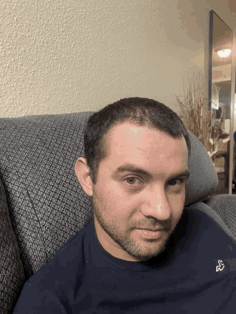 a man is sitting on a couch wearing a blue shirt with a bird on it