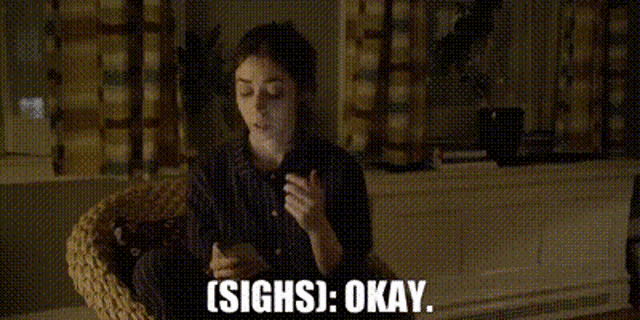 a woman is sitting in a wicker chair holding a cell phone and saying `` sighs okay '' .