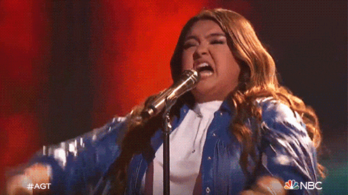 a woman singing into a microphone with a nbc logo behind her