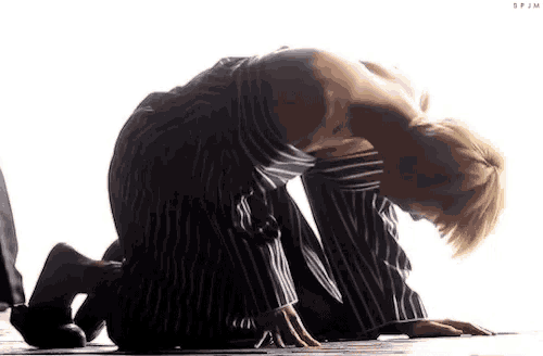 a man in a striped shirt is kneeling on the floor with his head down .