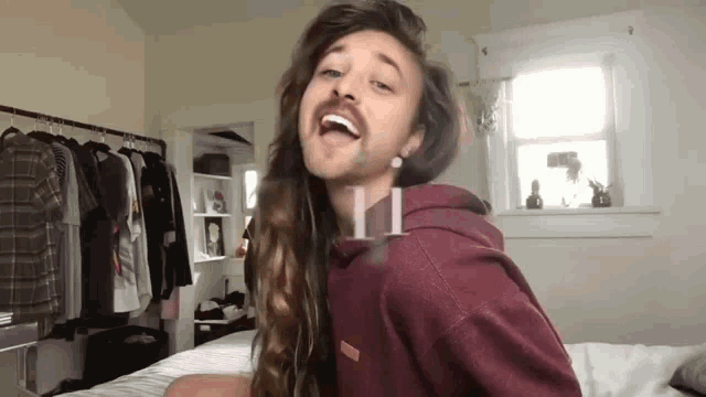 a young man with long hair and a beard is sitting on a bed .