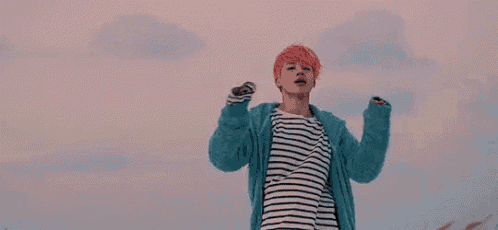 a young man with pink hair is standing in front of a pink sky .