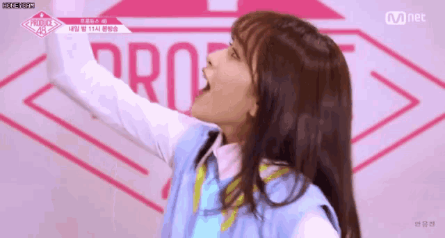 a girl in a blue vest and white shirt is standing in front of a pink logo .