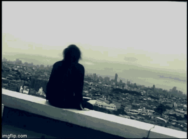a silhouette of a person sitting on a ledge overlooking the city