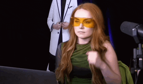 a woman with red hair is wearing a green dress and orange glasses .