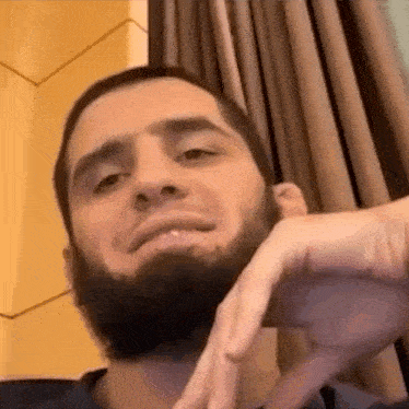 a man with a beard is making a funny face while sitting in front of a window .
