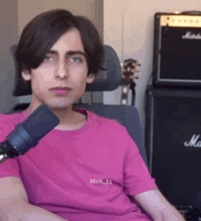 a young man is sitting in front of a microphone wearing a pink shirt .