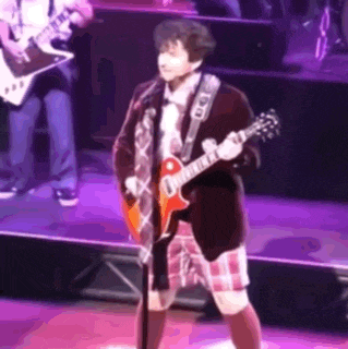 a man in a kilt is playing a guitar and singing into a microphone on a stage .