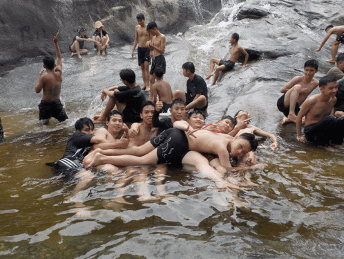 a group of young men are laying in the water and one of them is wearing a black shirt that says ' adidas '