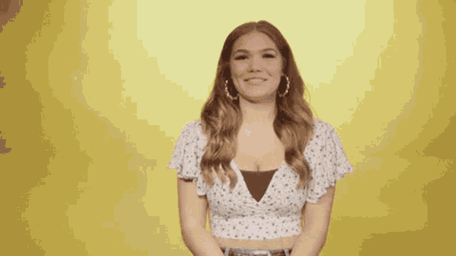 a woman in a white polka dot top is clapping her hands against a yellow background .