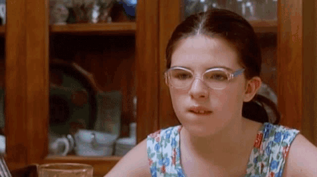a young girl wearing glasses is sitting at a table with a glass of water