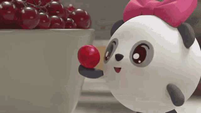 a cartoon panda bear is holding a red ball in front of a bowl of cherries .