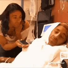 a woman is standing next to a man in a hospital bed looking at his cell phone .
