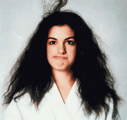 a woman with messy hair is wearing a white robe and making a face .