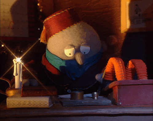 a stuffed animal wearing a red hat and scarf sits on a table next to a candle