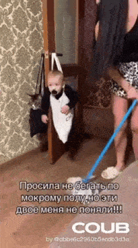 a baby with a pacifier in his mouth is being held by a woman while a woman holds a mop .