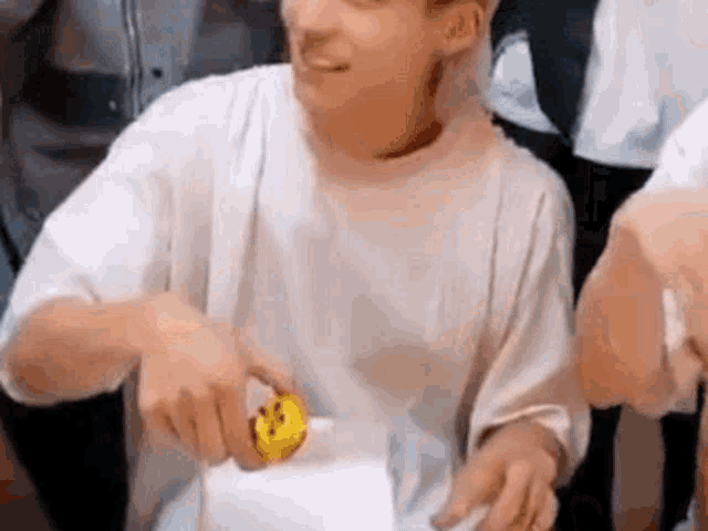 a man in a white shirt is sitting at a table holding a yellow smiley face .