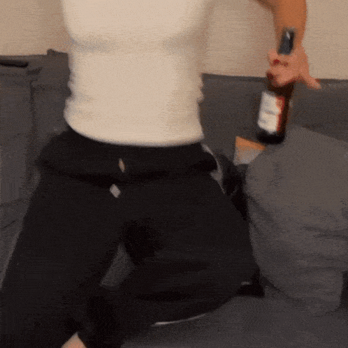 a person is kneeling on a couch holding a bottle of alcohol