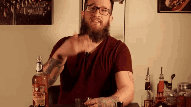 a man with a beard and glasses is sitting at a table with a bottle of valort whiskey