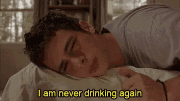 a young man is laying on a bed with his eyes closed and says `` i am never drinking again '' .