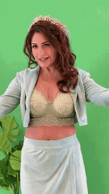 a woman wearing a crop top and a skirt is standing in front of a green background