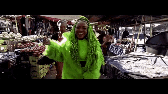 a woman with green hair is standing in front of a fruit stand .